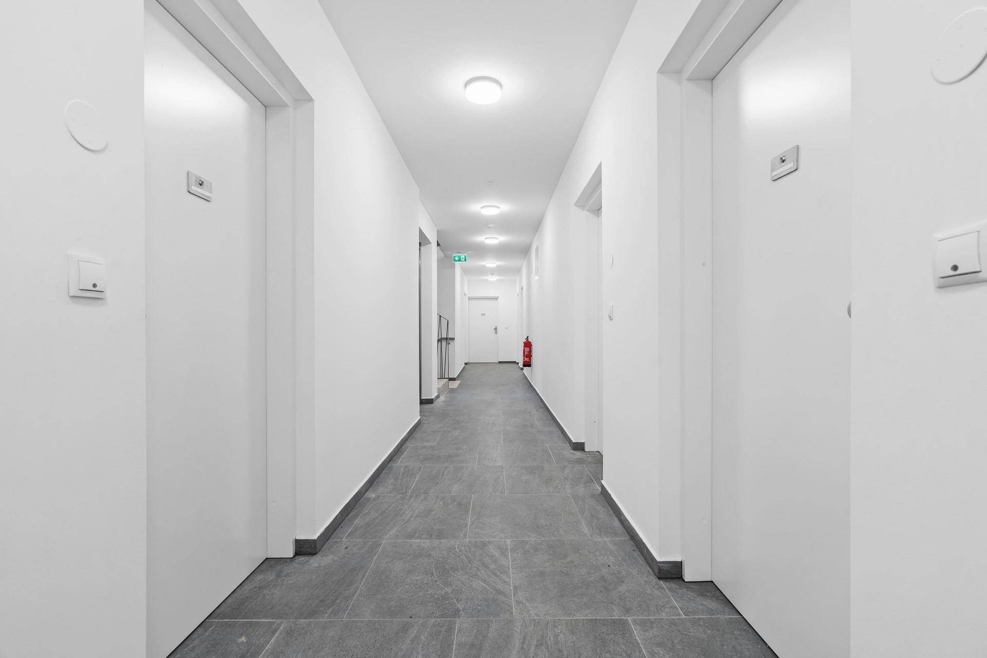 Langer, heller Flur im Gemeinschaftsbereich mit mehreren Wohnungstüren und Fliesenboden.
