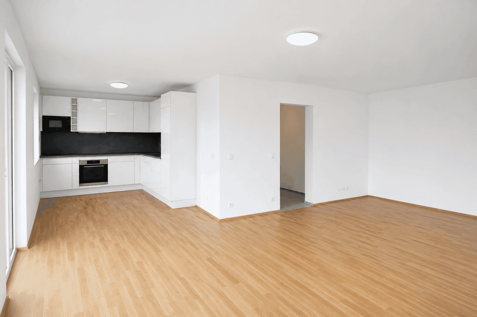 Offener Wohnbereich mit Holzboden und integrierter, moderner weißer Küche mit dunkler Rückwand.