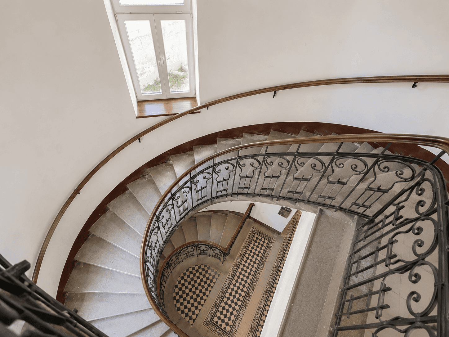 Elegantes Treppenhaus mit schmiedeeisernem Geländer und gemusterten Fliesenböden von oben gesehen.
