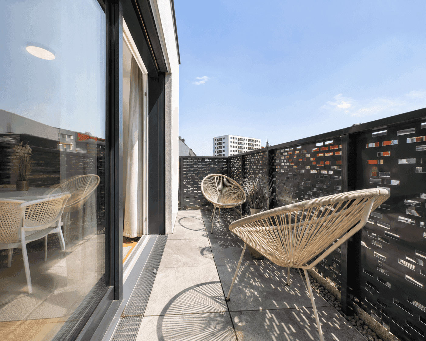 Sonniger Balkon mit modernen Outdoor-Sesseln und dekorativer Sichtschutzwand.