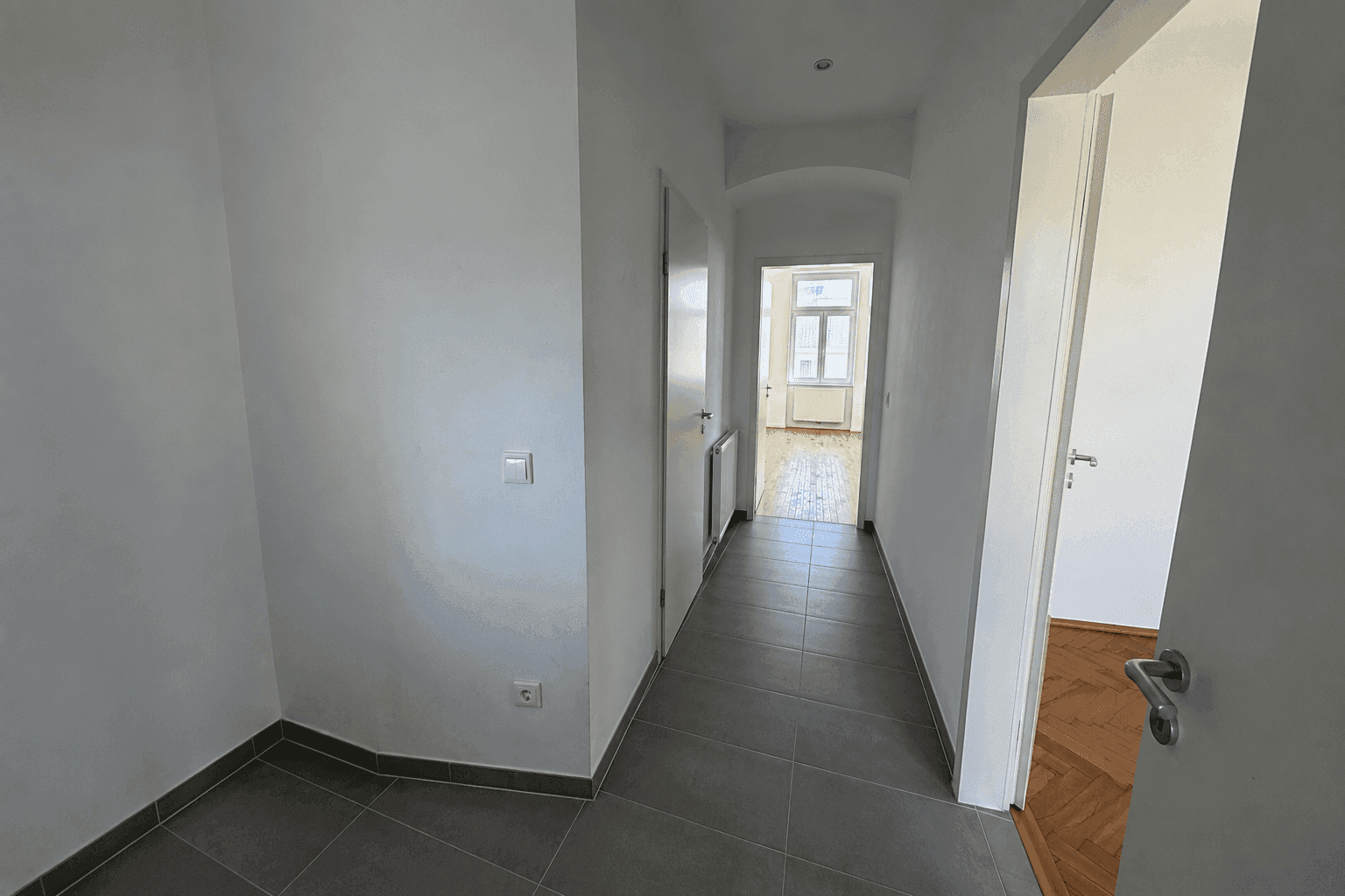 Heller Flur mit modernen grauen Fliesen und Blick in angrenzende Zimmer mit Parkett.
