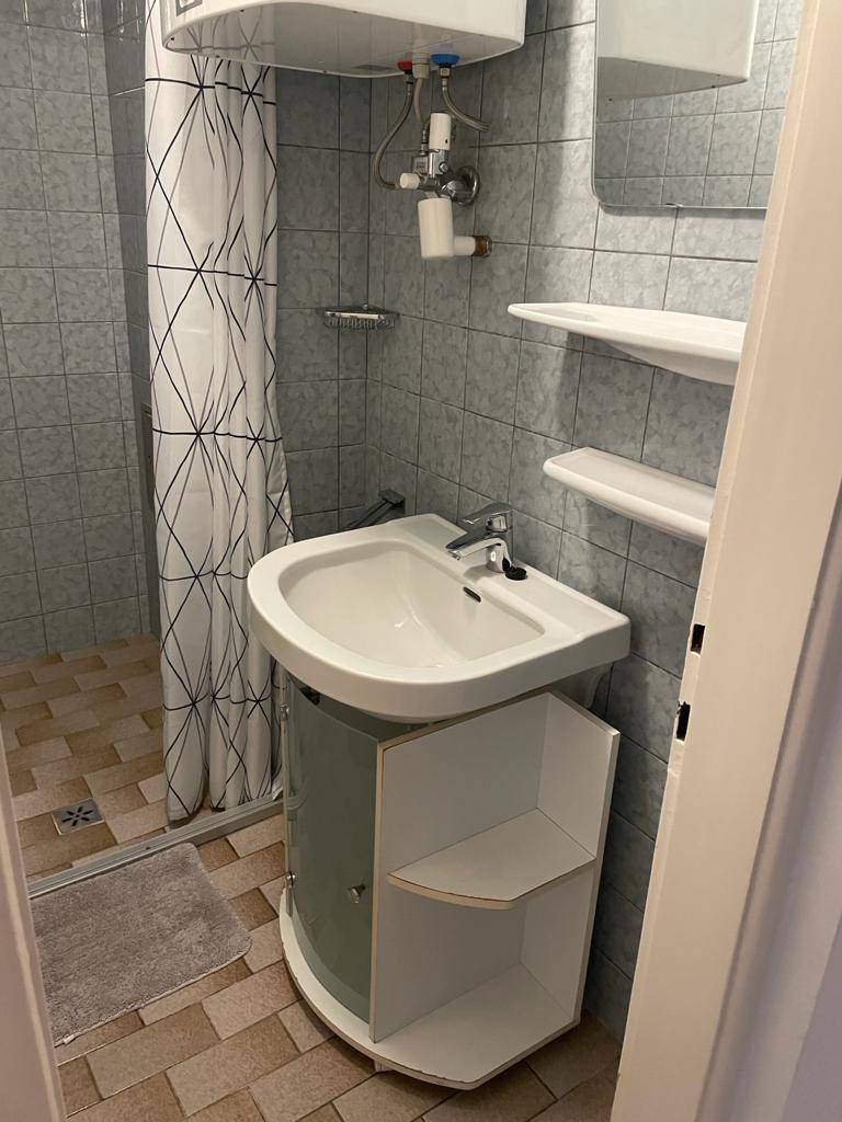 Kleines Badezimmer mit Dusche, Waschbecken und grauen Fliesen.