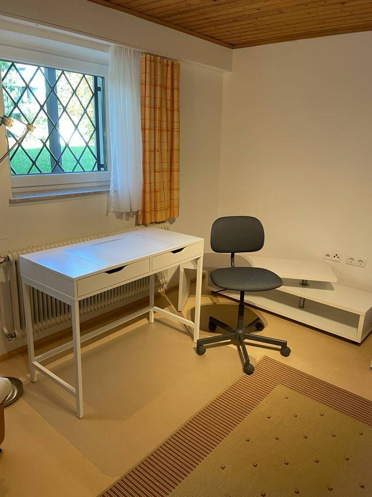 Funktionaler Arbeitsbereich mit weißem Schreibtisch, Bürostuhl und Blick ins Grüne durch das Fenster.