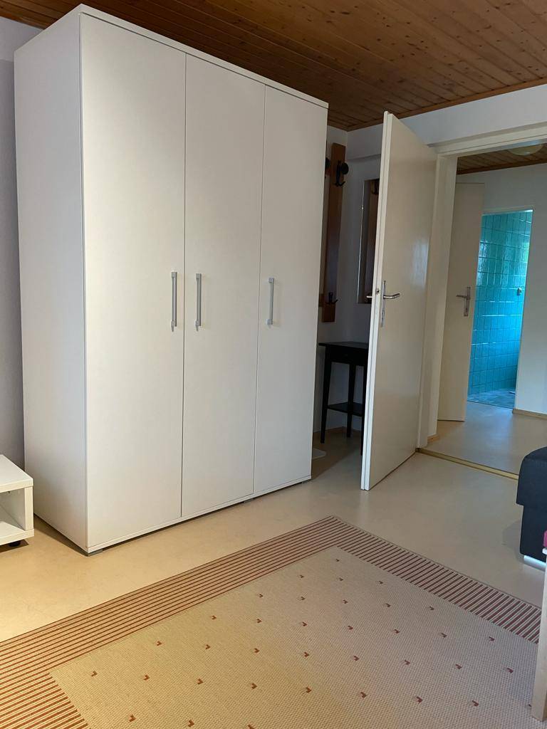 Schlafzimmer mit großem weißen Kleiderschrank und Holzbalkendecke, angrenzend an ein Badezimmer.