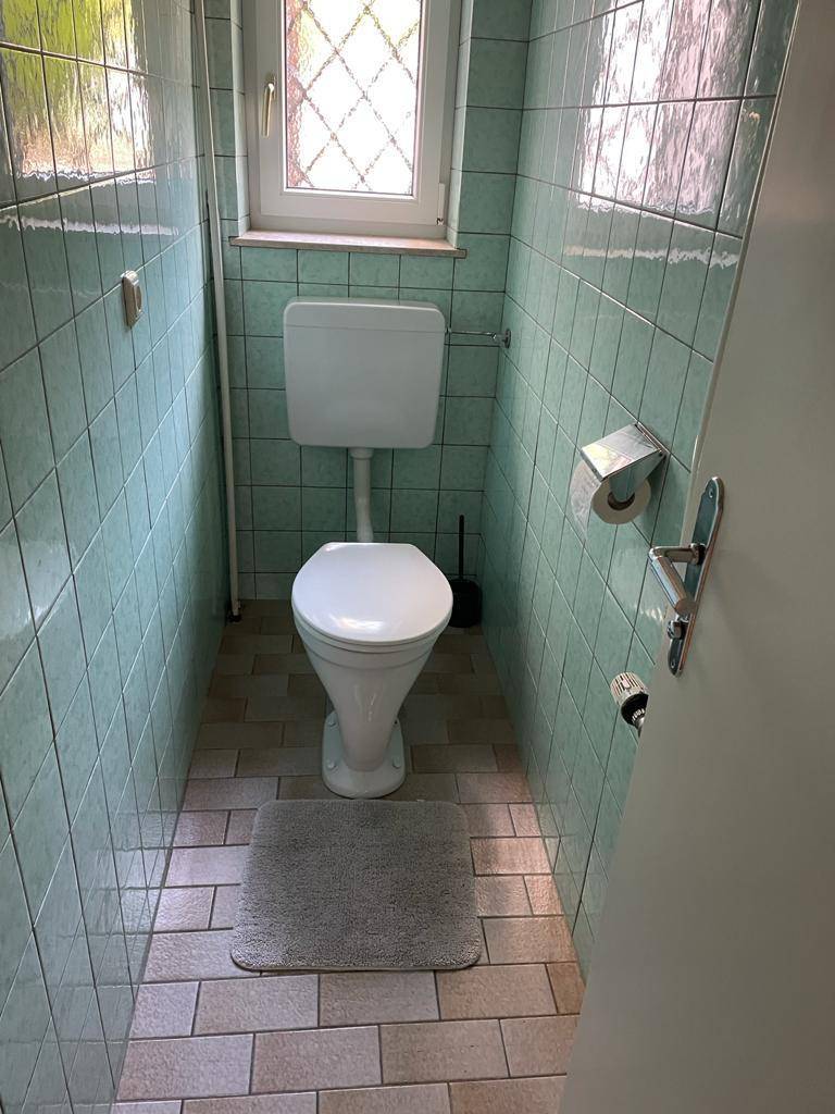 Separates WC mit Toilette, Fenster und hellgrünen Wandfliesen.