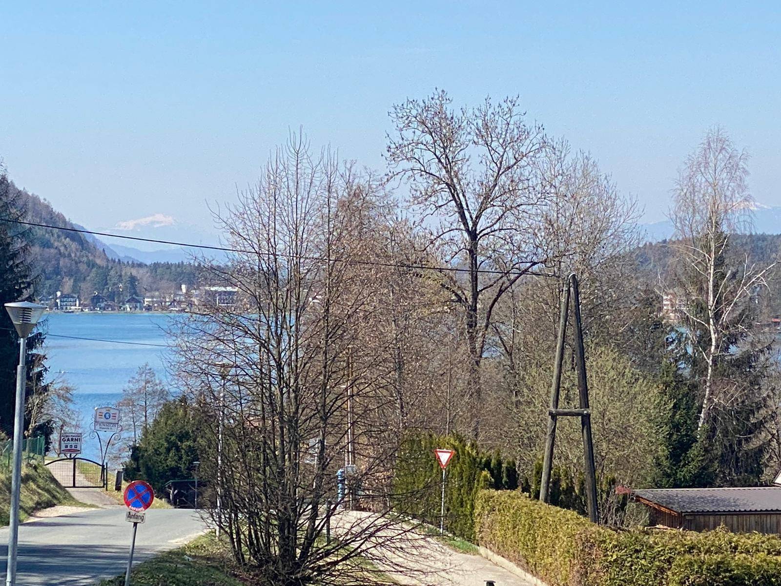 Weitläufiger Blick über den See und die bewaldeten Hügel mit schneebedeckten Berggipfeln im Hintergrund.