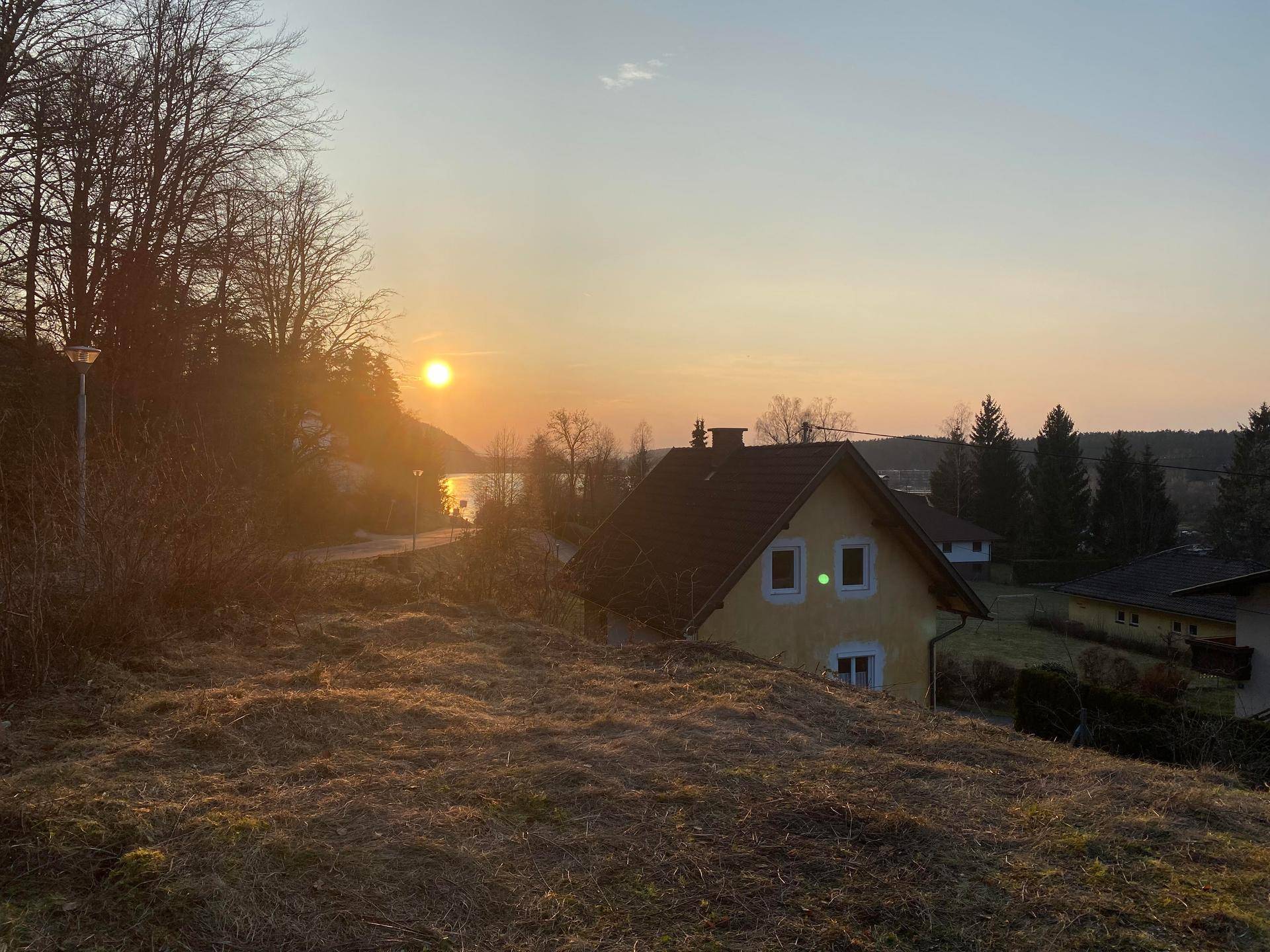 Gelbes Wohnhaus auf einem Hügel mit Blick auf einen See bei Sonnenuntergang und umliegender Natur.