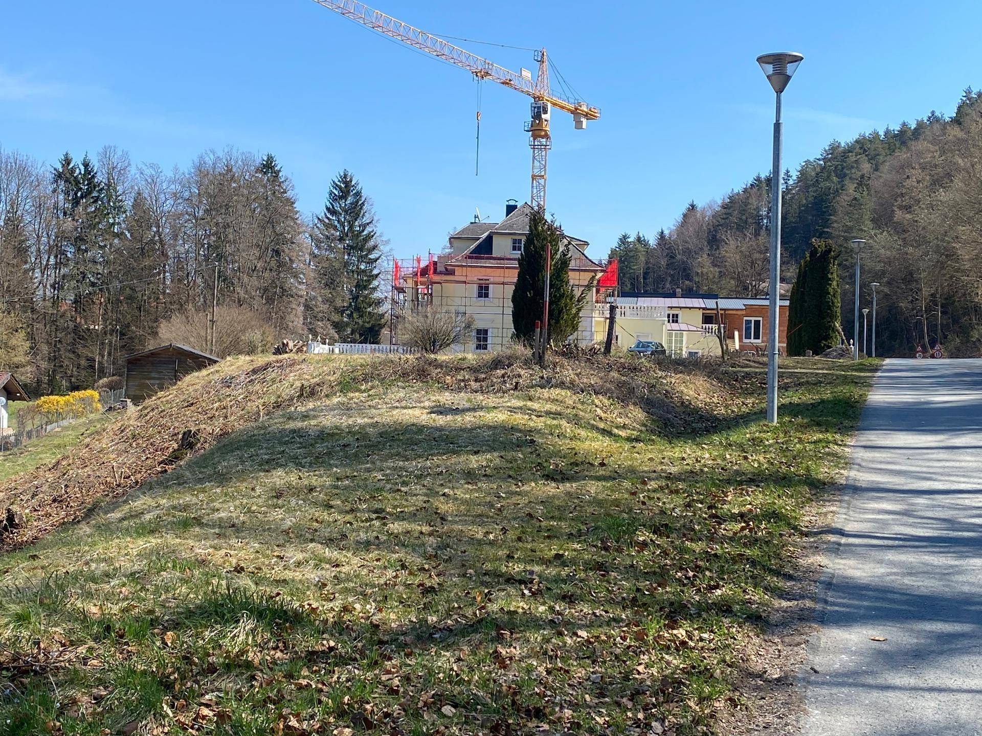 Hanglage des Grundstücks mit Straße, Baustelle und Kran im Hintergrund, umgeben von Wald.
