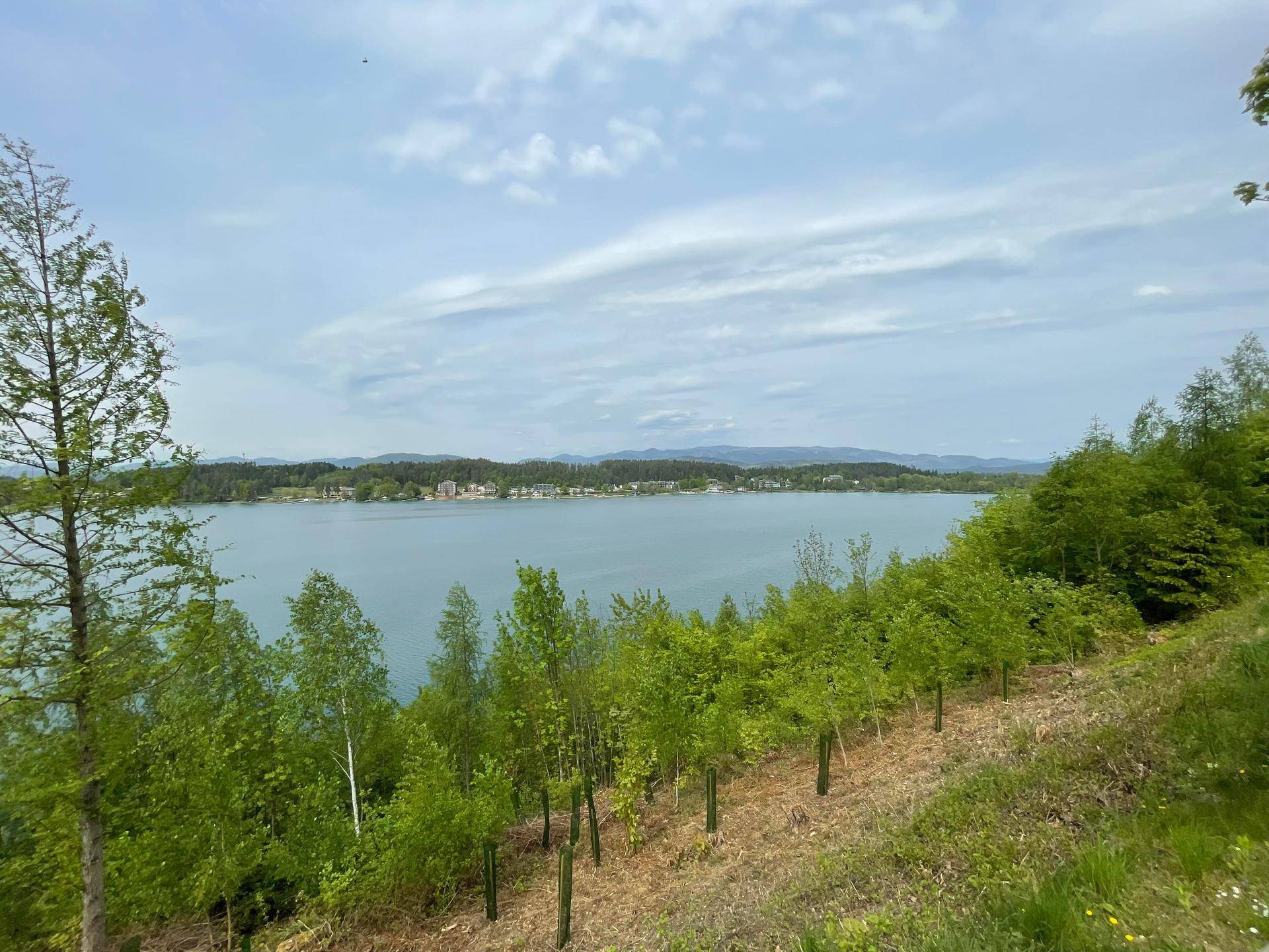 Weitläufiger Blick über einen ruhigen See mit bewaldeten Ufern und einer kleinen Siedlung am Horizont.