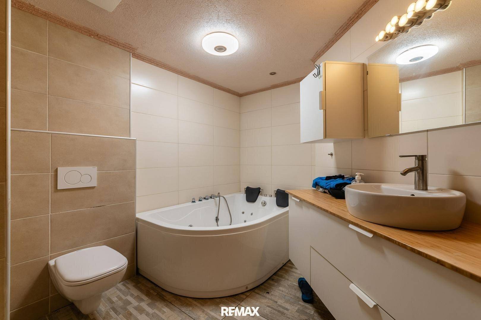 Modernes Badezimmer mit Eckbadewanne, Waschtisch und Wand-WC, hell gefliest.