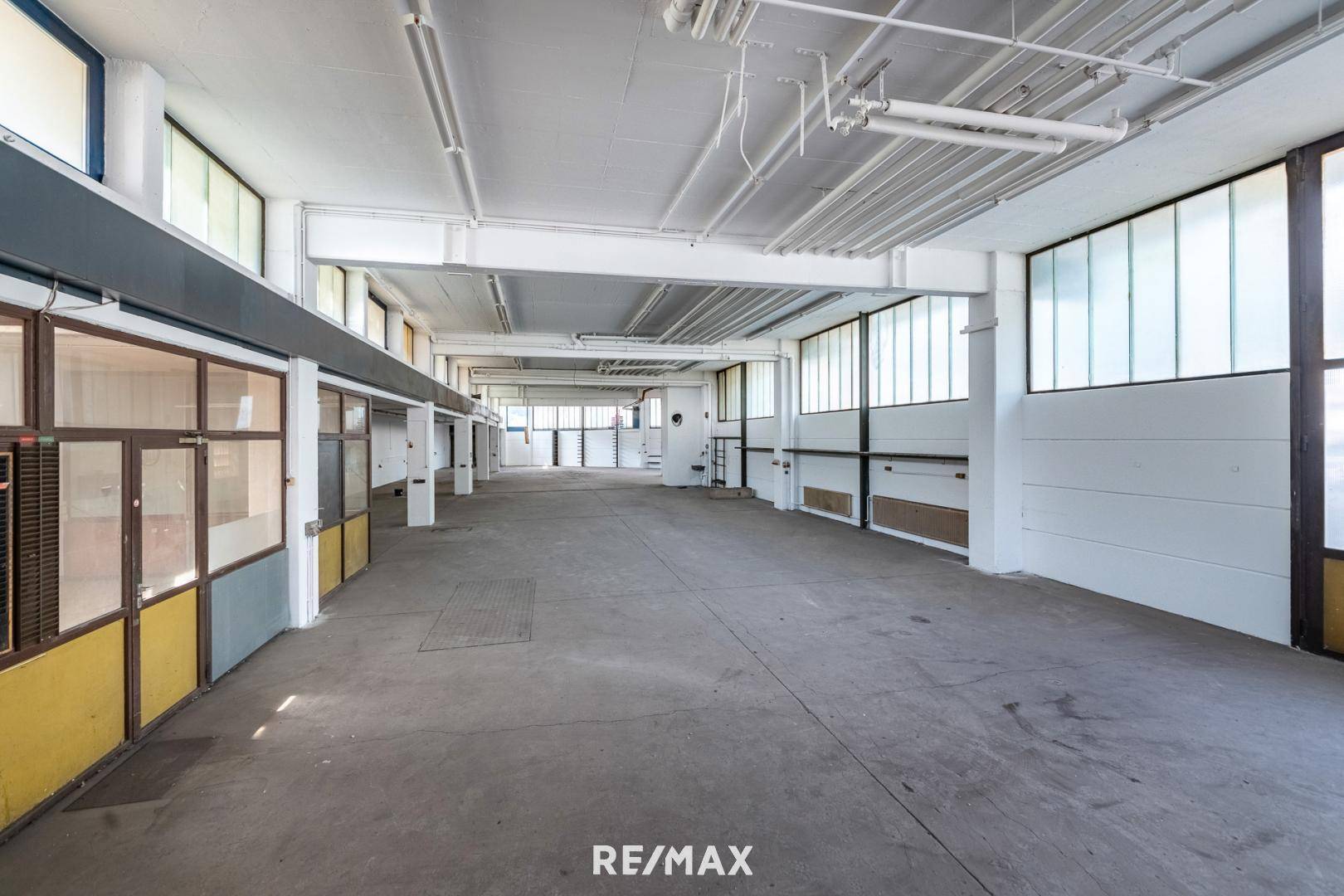 Langer, offener Gewerberaum mit Betonboden, hohen Decken und vielen Fenstern, ideal für flexible Nutzung.