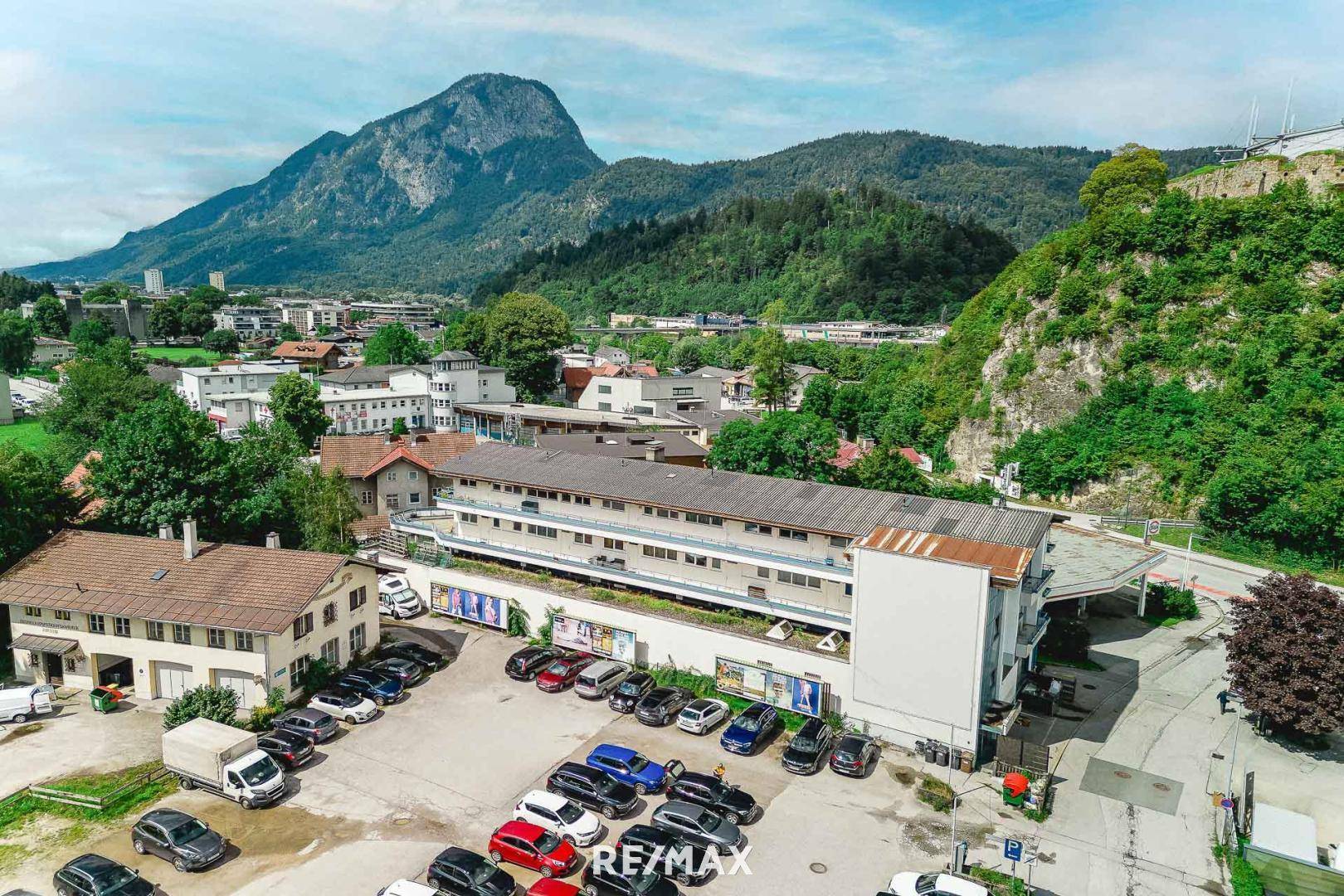 Weitläufige Luftaufnahme eines Gewerbegebäudes mit Parkplätzen, umgeben von Bergen und grüner Landschaft.