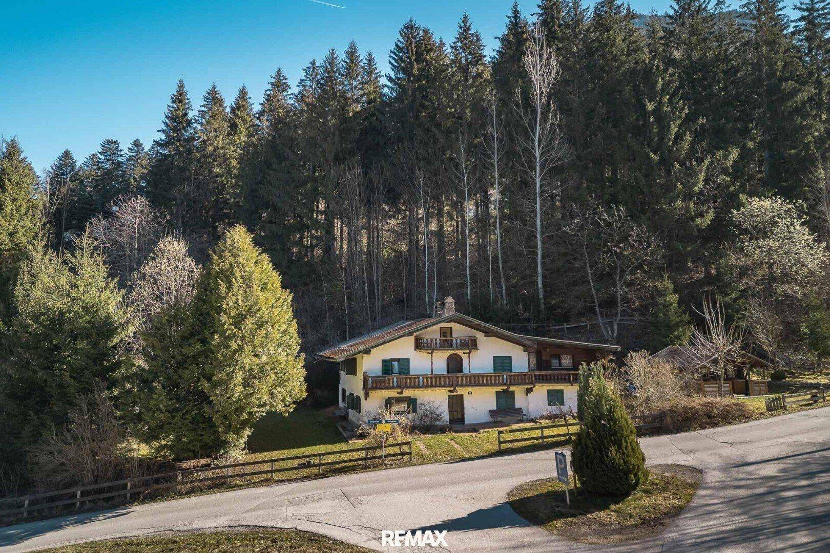 Traditionelles Haus im Grünen, eingebettet in eine bewaldete Berglandschaft mit sonnigem Grundstück.