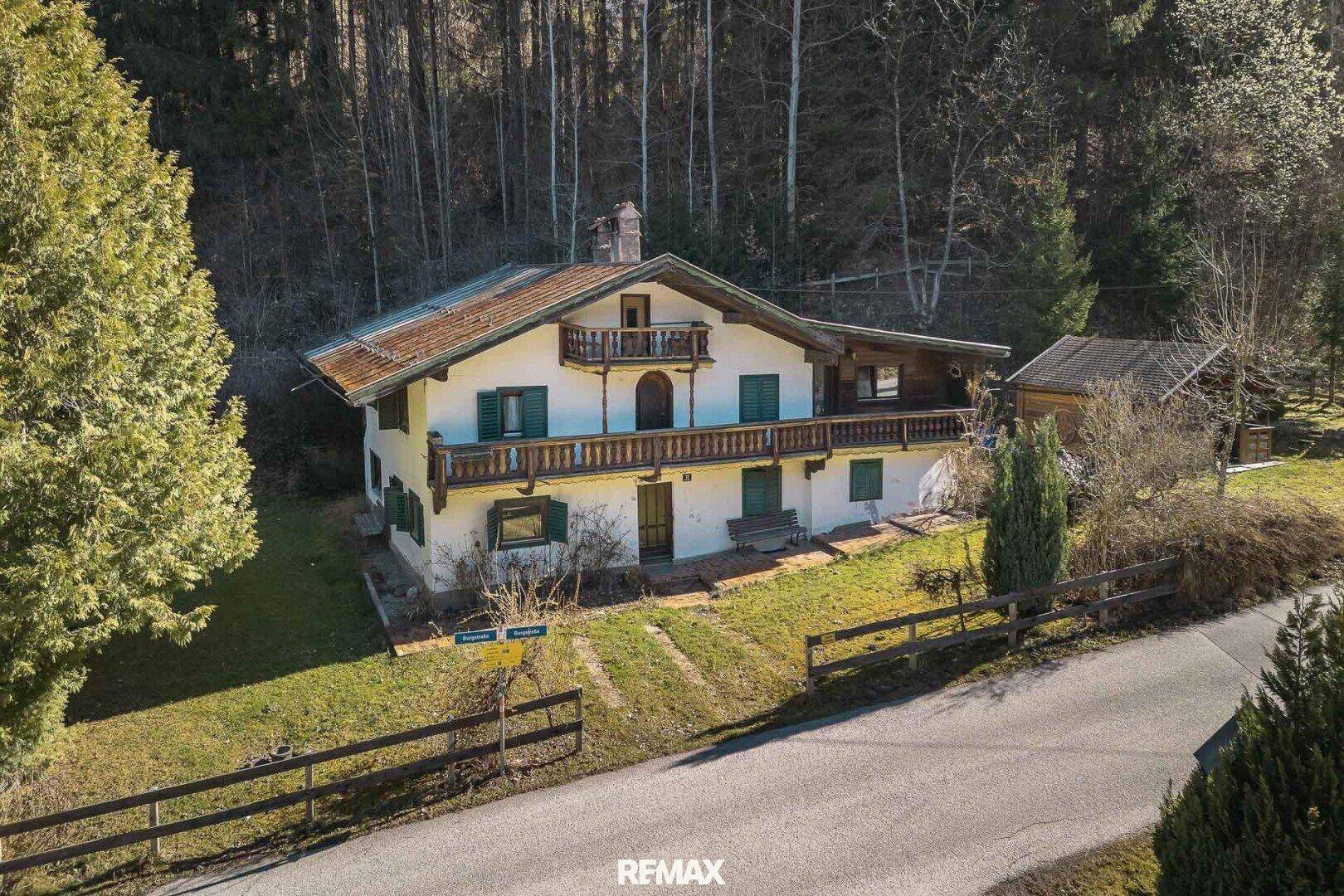Alpines Wohnhaus mit Holzbalkonen und grünen Fensterläden, umgeben von einem gepflegten Garten.