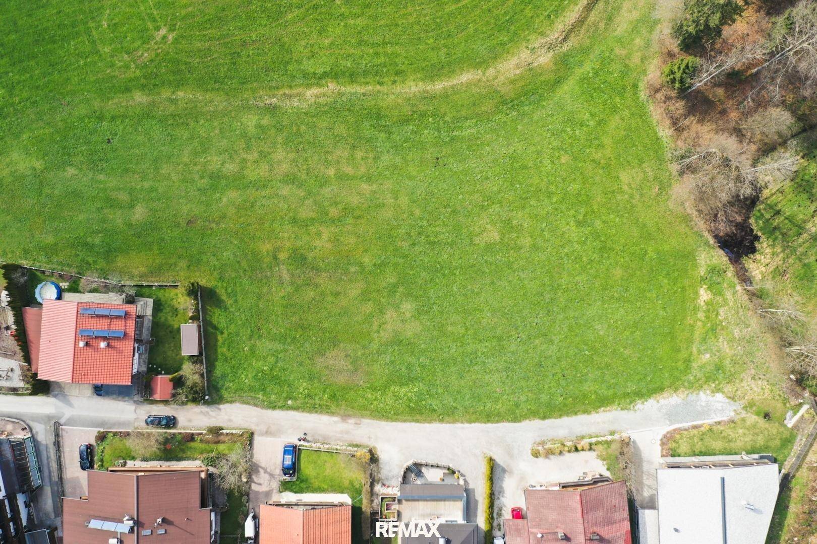 Luftaufnahme eines großen grünen Grundstücks, umgeben von einer Straße und angrenzenden Häusern.