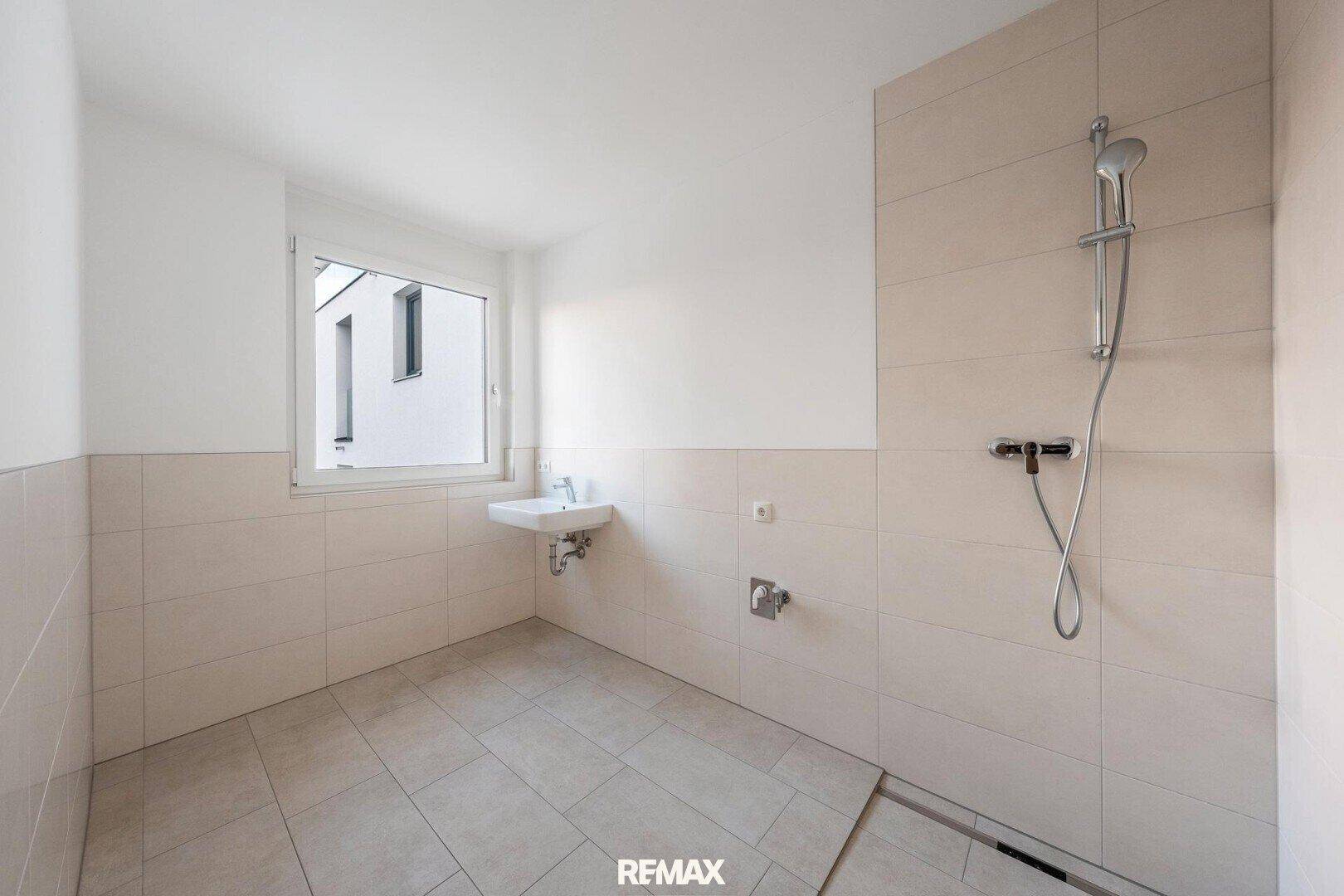Modernes Badezimmer mit begehbarer Dusche, kleinem Waschbecken und Fenster.