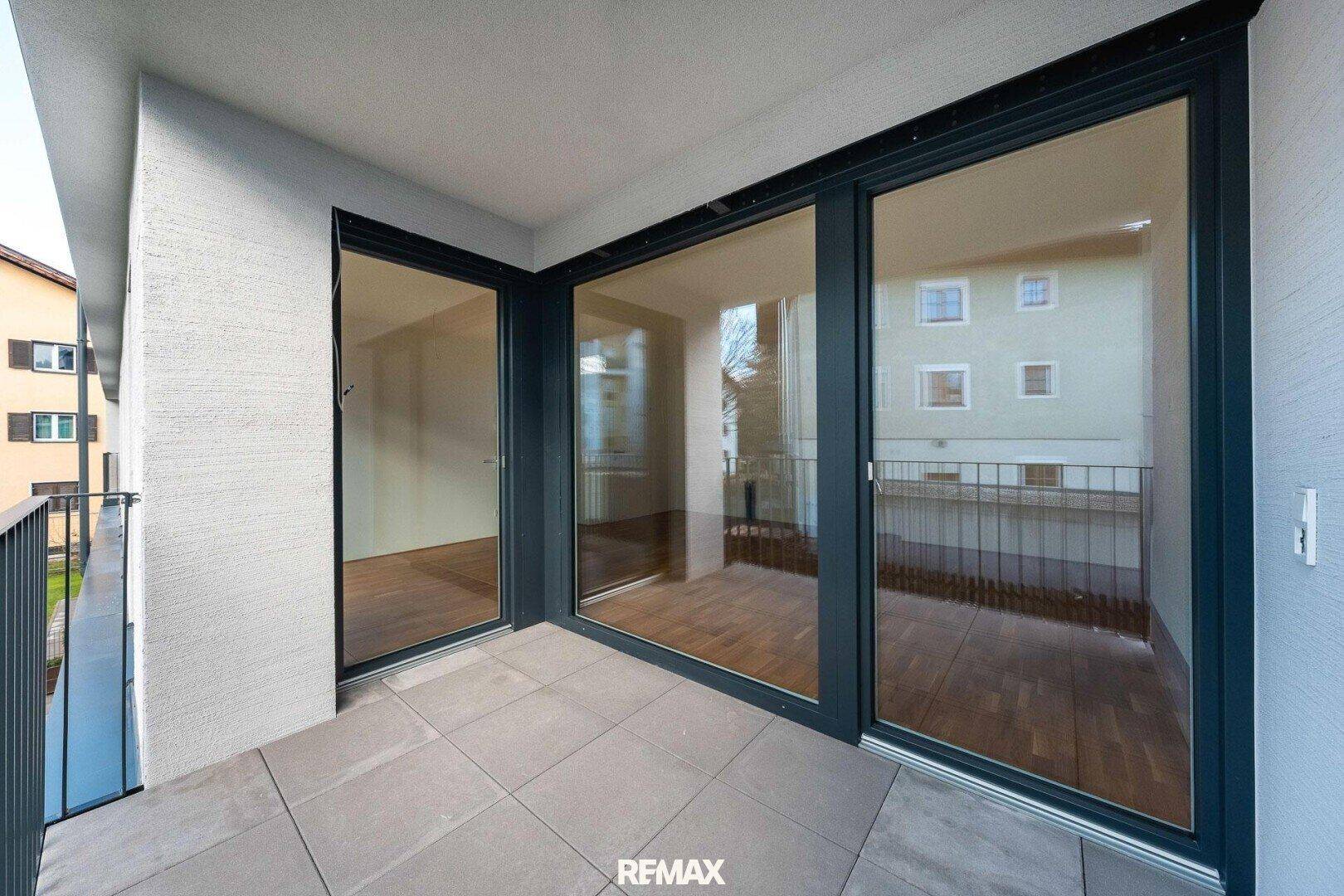 Moderner Balkon mit Fliesenboden und großen Glasfronten, die den Innenraum erweitern.