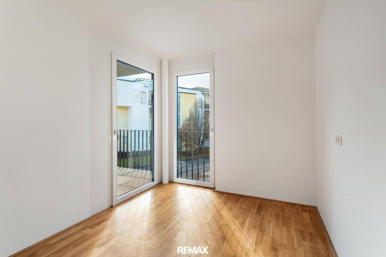 Schlafzimmer mit Holzboden und zwei Fenstertüren, die viel Tageslicht hereinlassen.