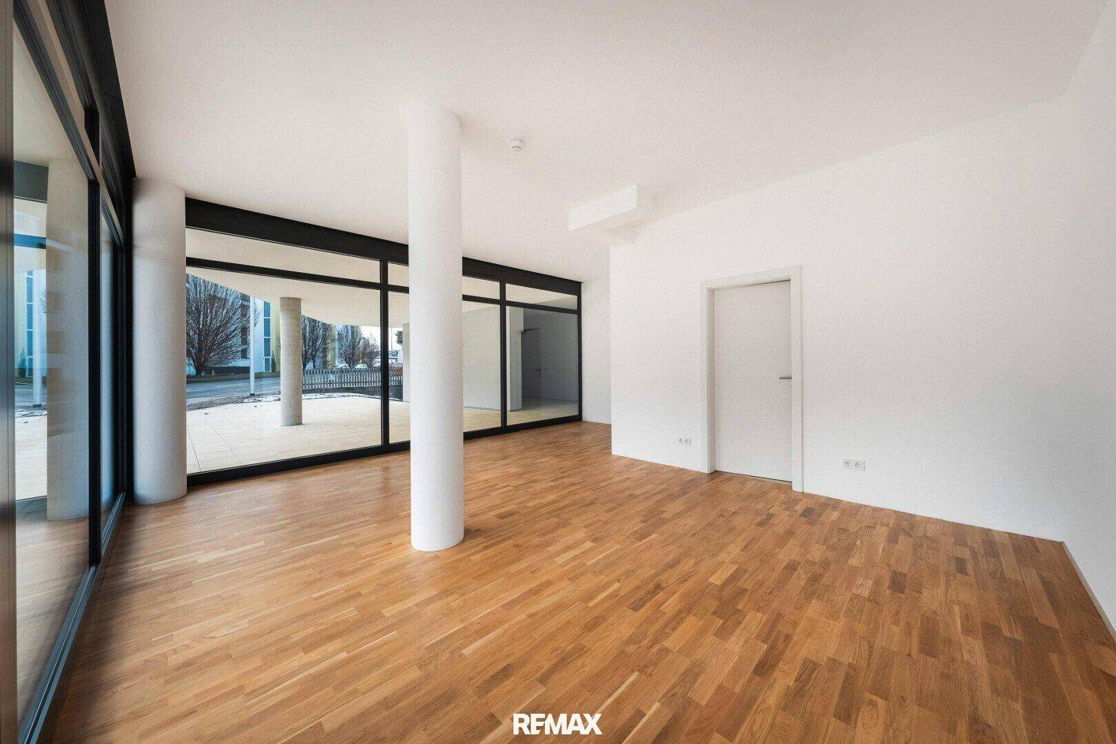 Heller, leerer Raum mit Holzboden und raumhohen Fenstern, ideal für ein Büro oder Geschäft.