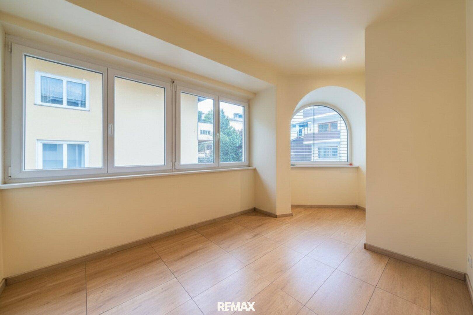 Geräumiges Zimmer mit großen Fenstern und einem dekorativen Rundbogenfenster, gefliestem Boden.
