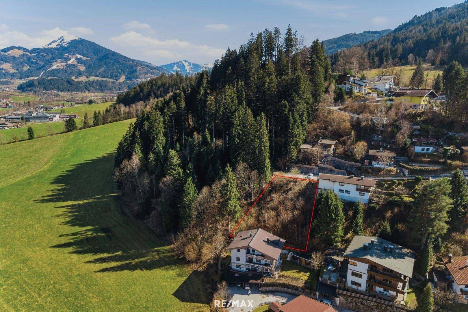 Weitläufige Luftaufnahme eines Baugrundstücks in idyllischer Lage mit Bergblick und Wiesen.