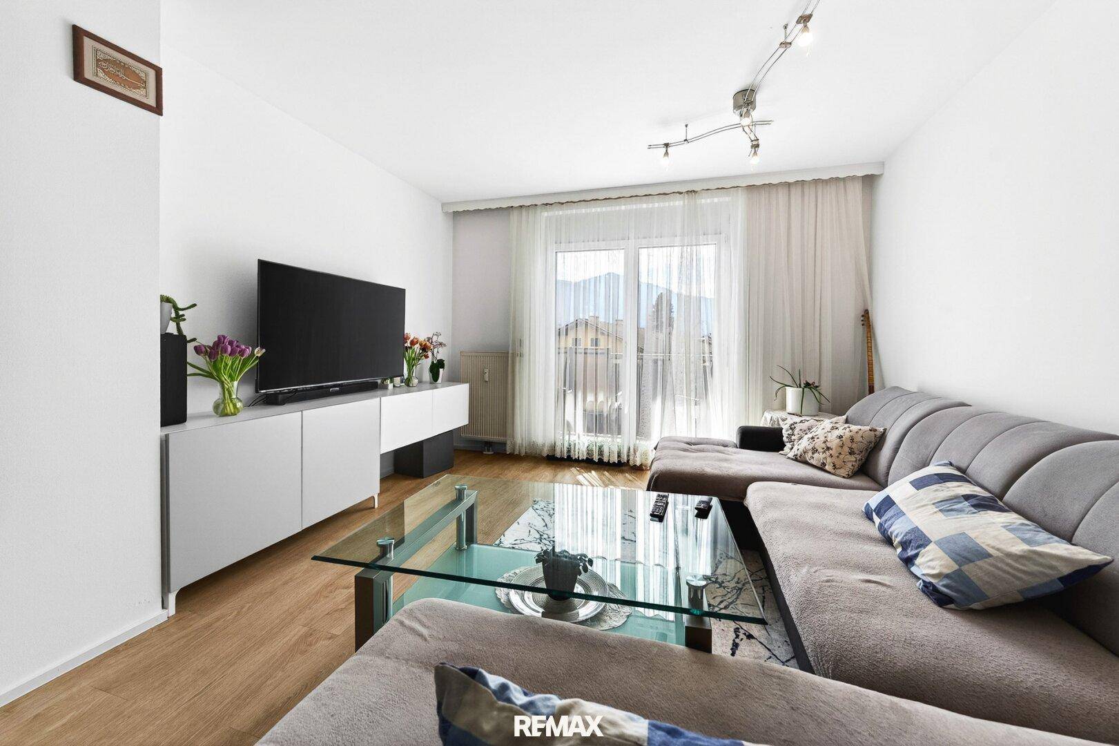 Helles Wohnzimmer mit großem Sofa, Couchtisch und Zugang zum Balkon, mit Blick auf die Berge.