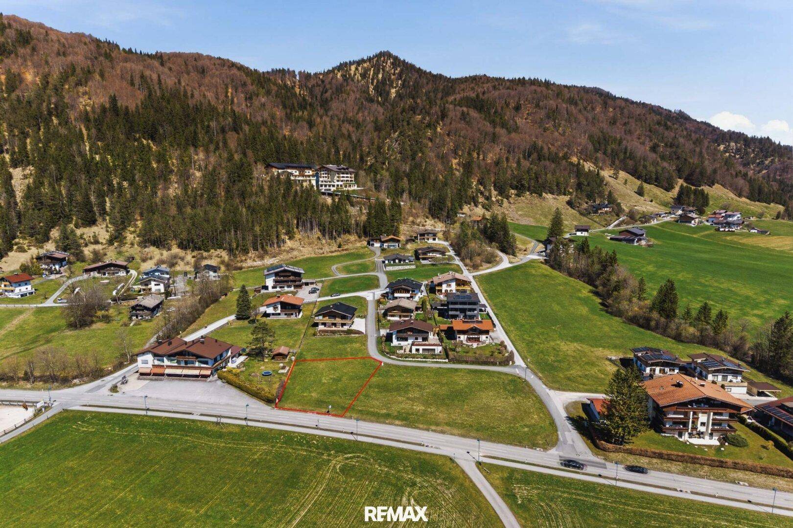 Luftaufnahme des Baugrundstücks in einer Wohngegend mit Blick auf bewaldete Berge.