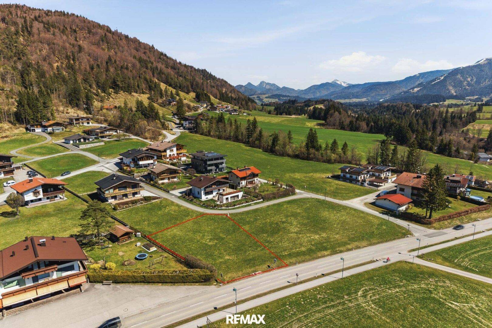 Übersicht des Baugrundstücks an einer Straße, umgeben von grünen Wiesen und Bergen.
