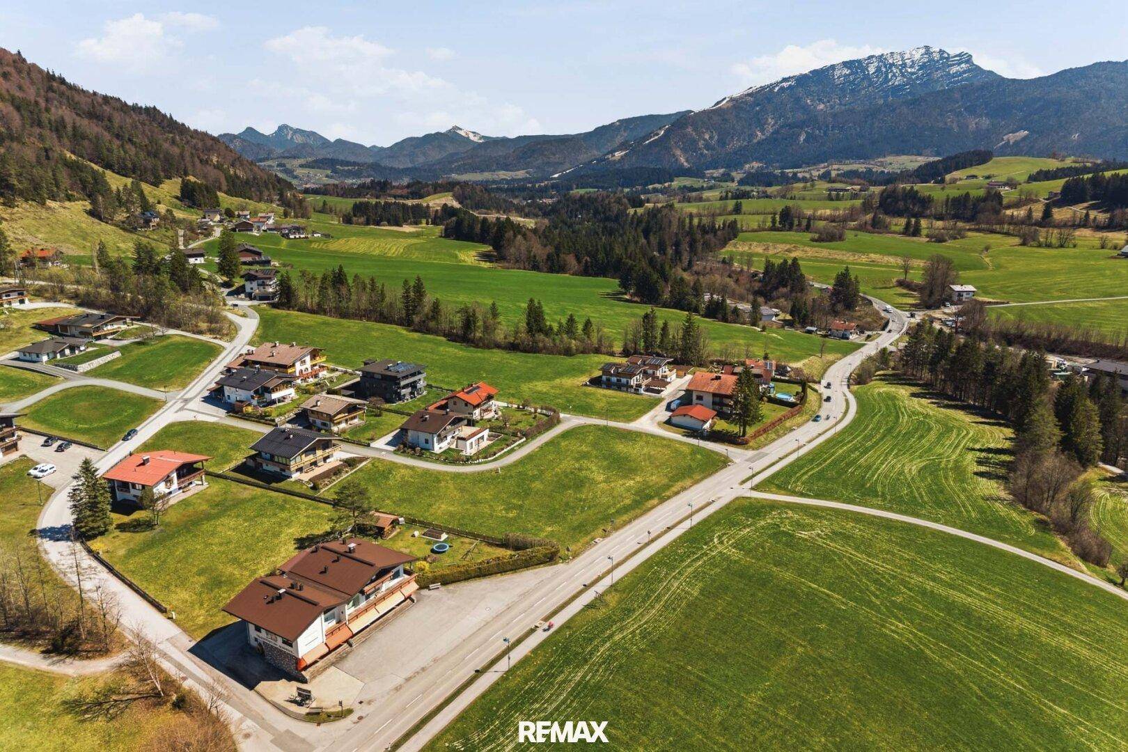Weitläufige Ansicht des Baugrundstücks innerhalb einer ländlichen Siedlung mit Bergpanorama.