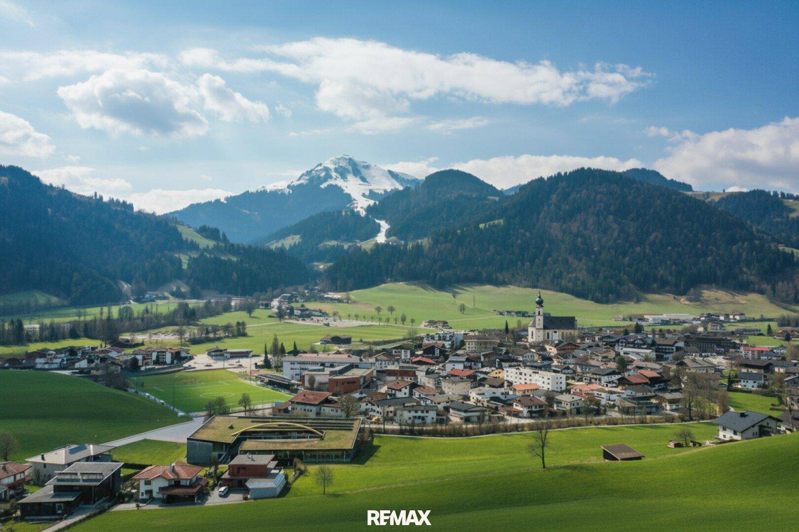 Weitwinkelaufnahme eines charmanten Dorfes eingebettet in eine beeindruckende Bergkulisse mit schneebedeckten Gipfeln.