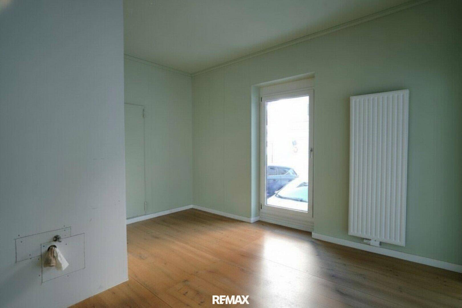 Leerer Raum mit warmem Holzboden, einem Fenster und einem Heizkörper an der Wand.