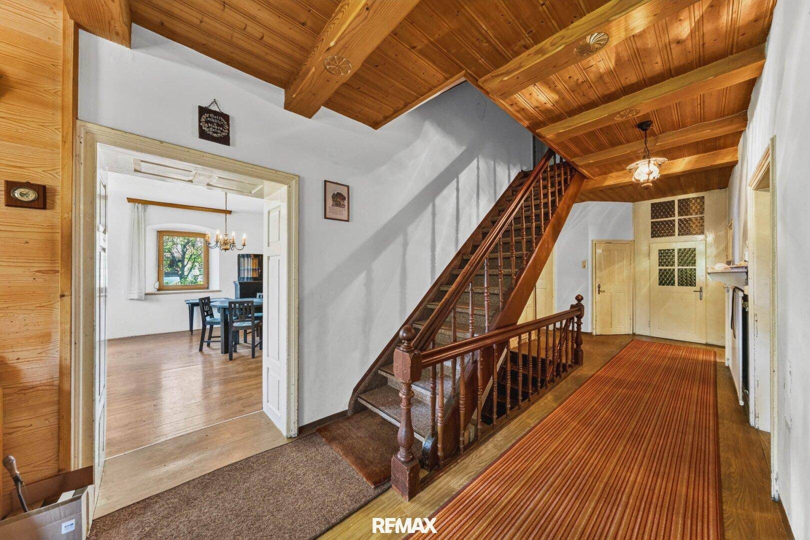 Geräumiger Flur mit einer Holztreppe, Holzbalkendecke und Zugang zu weiteren Zimmern im Haus.