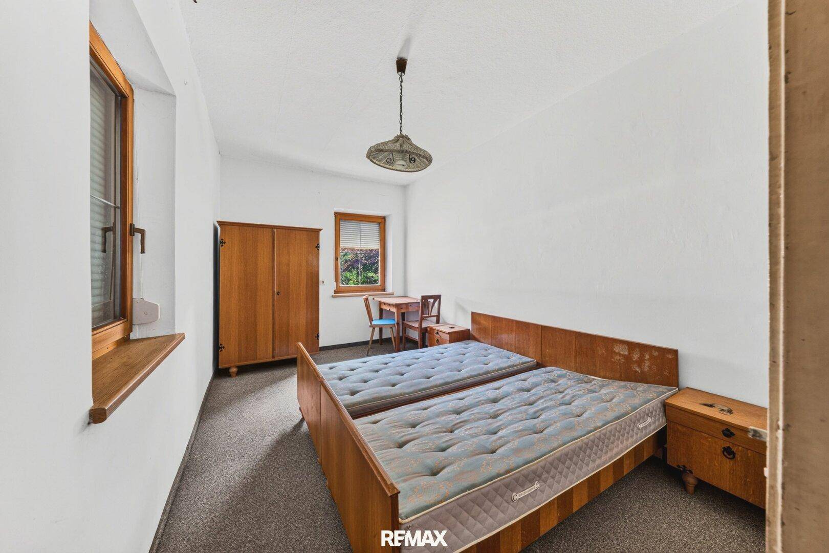 Helles Schlafzimmer mit zwei Einzelbetten, einem Holzschrank und einem Fenster mit Blick ins Grüne.