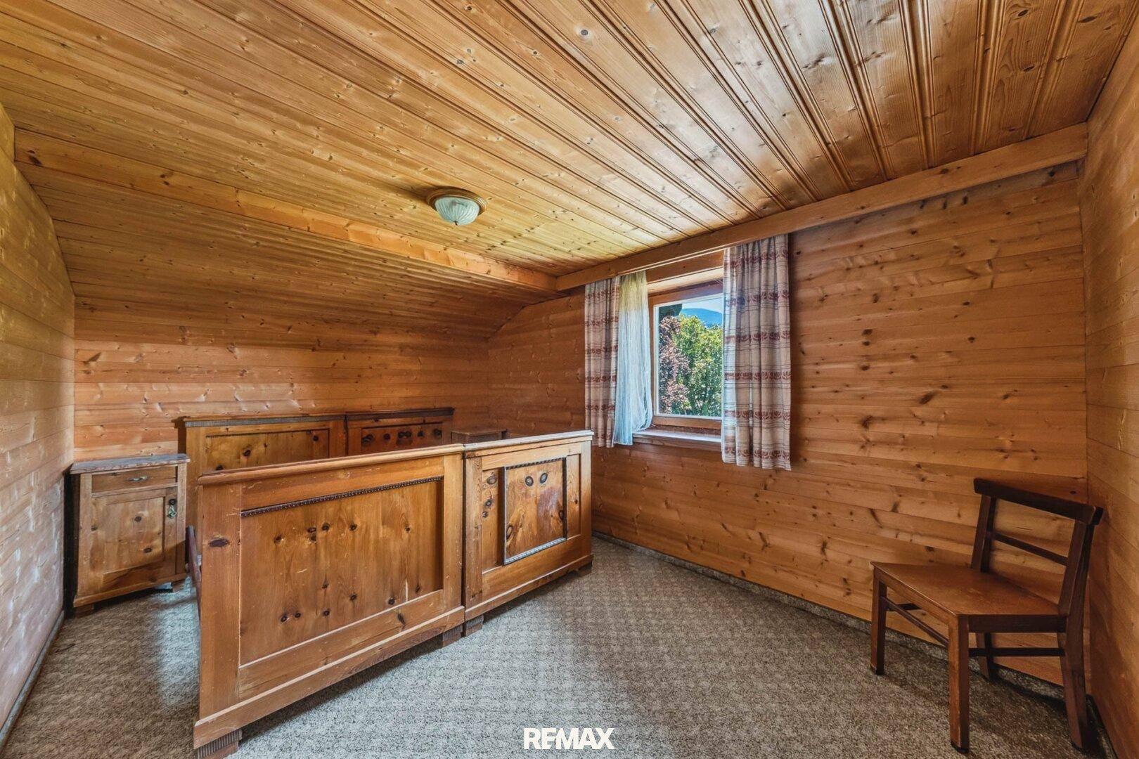 Gemütliches Schlafzimmer im Dachgeschoss mit Holztäfelung, Holzbett und einem Fenster mit Ausblick.