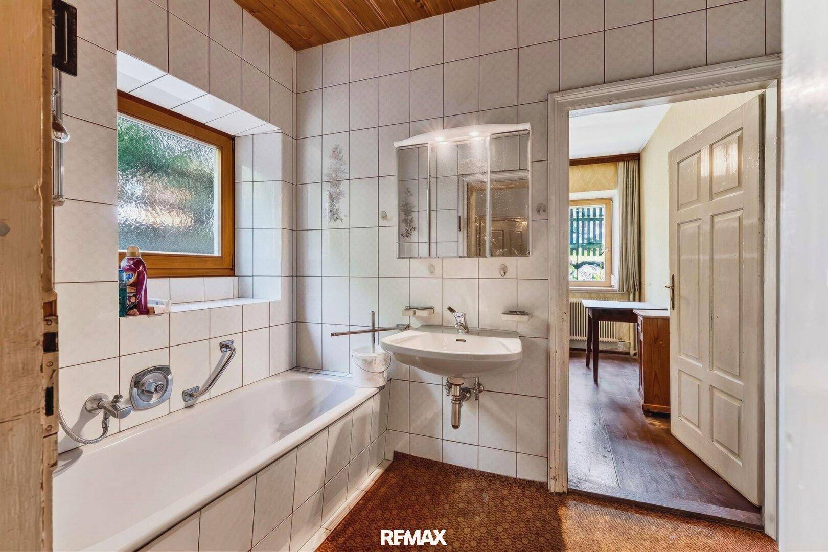Gefliestes Badezimmer mit Badewanne, Waschbecken und einem Fenster für Tageslicht.