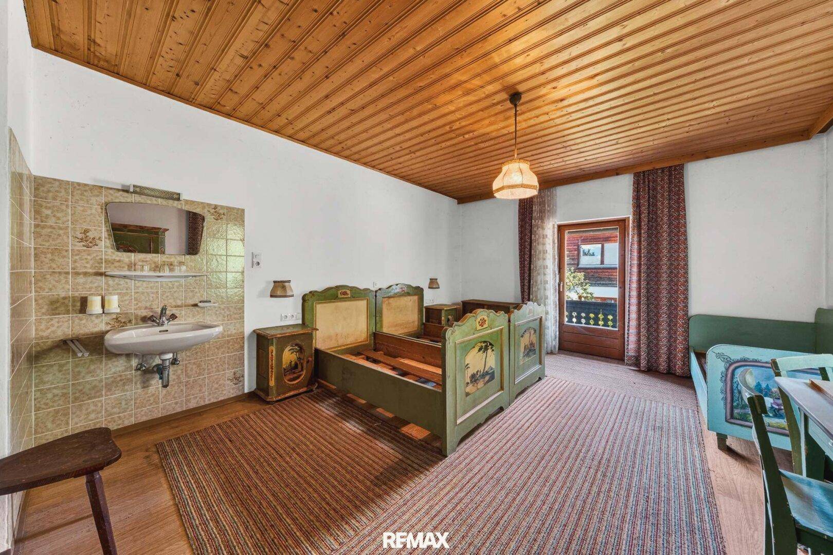 Schlafzimmer im alpinen Stil mit bemalten Holzbetten, Waschbecken und Balkonzugang.