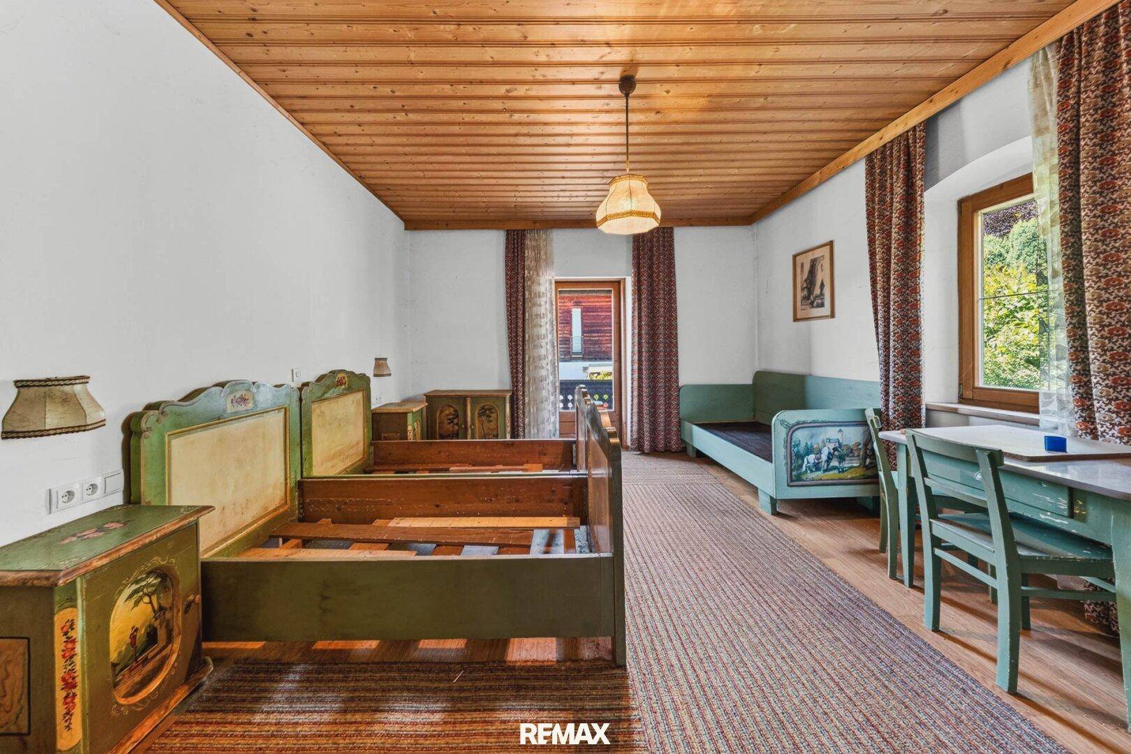 Traditionelles Schlafzimmer mit bemalten Holzbetten, Holzbalkendecke und Balkonzugang.