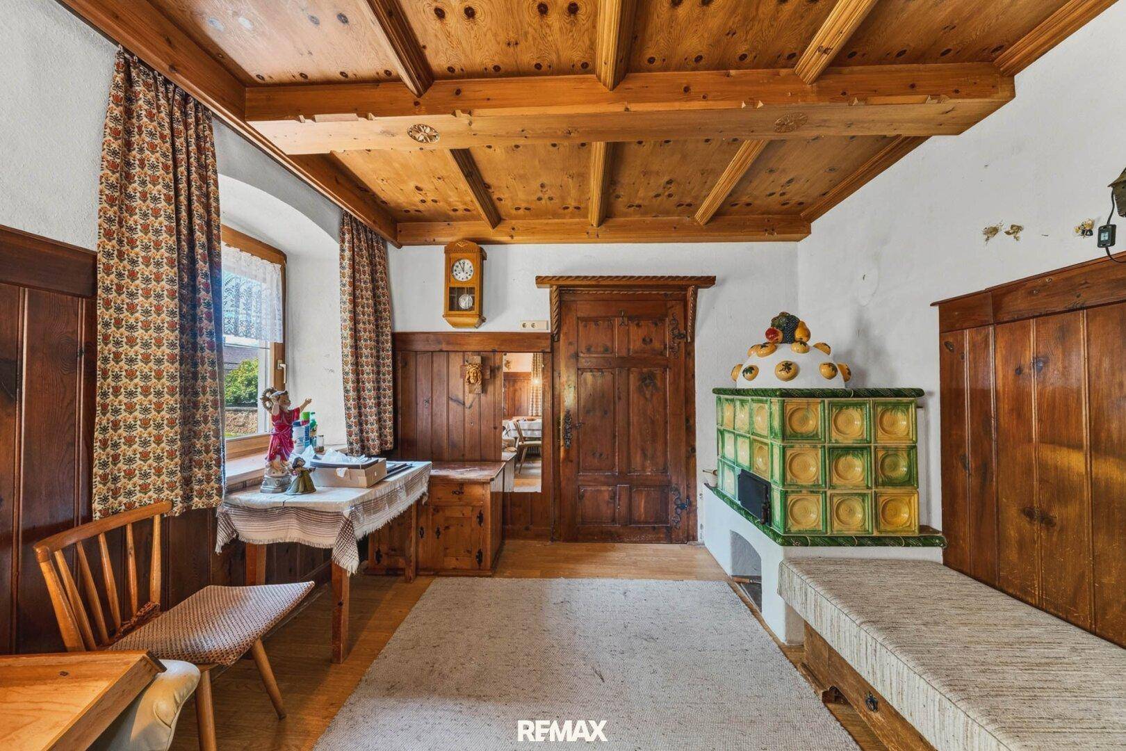 Gemütliches Wohnzimmer im alpinen Stil mit Kachelofen, Holzvertäfelung und Holzbalkendecke.