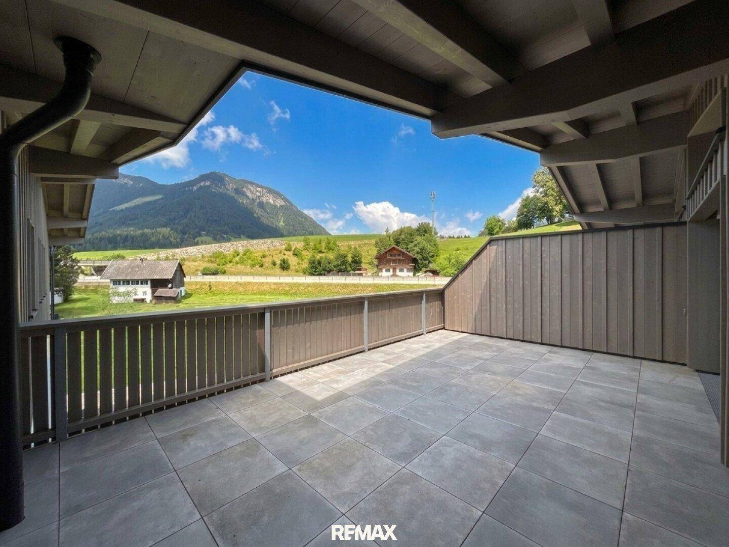 Weitläufige Terrasse mit Fliesenboden und Holzverkleidung, bietet einen atemberaubenden Blick auf die grüne Landschaft und Berge.