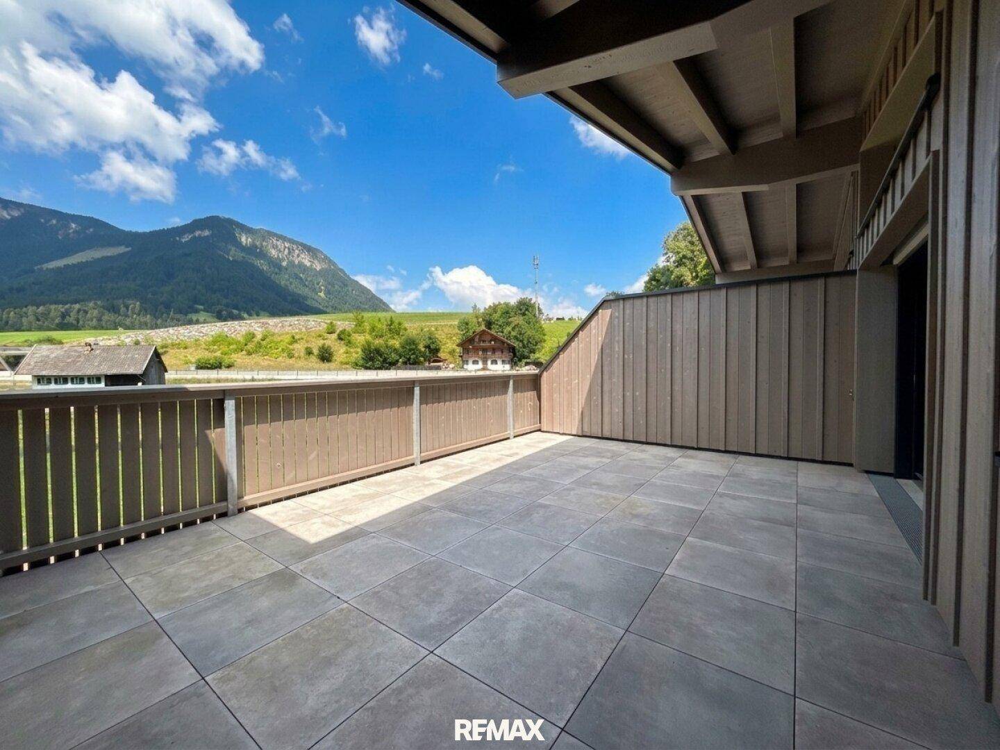 Sonnige Terrasse mit Fliesenboden und Holzgeländer, ideal zum Entspannen mit Panoramablick auf die Bergwelt.