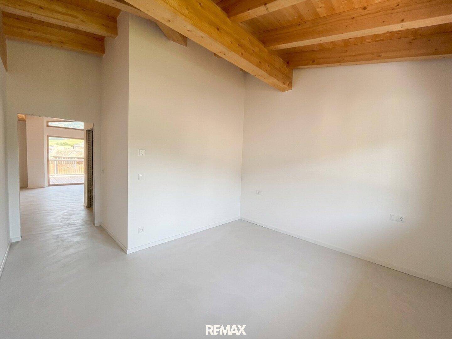 Helles Zimmer mit sichtbaren Holzdeckenbalken und Betonboden, ideal als Schlafzimmer oder Arbeitsbereich.