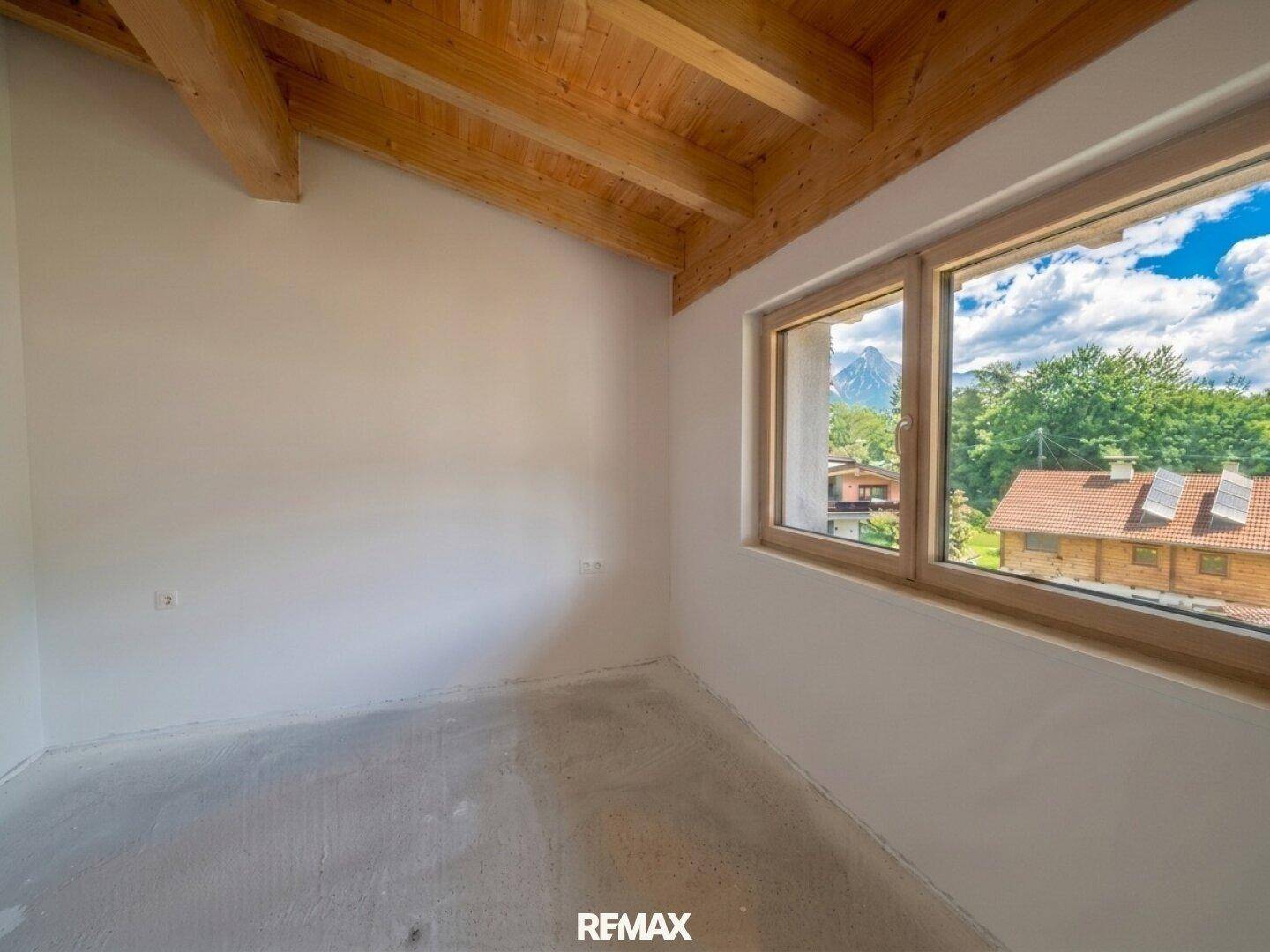 Gemütliches Zimmer mit Holzdeckenbalken und Betonboden, bietet einen schönen Ausblick auf die umliegenden Berge.