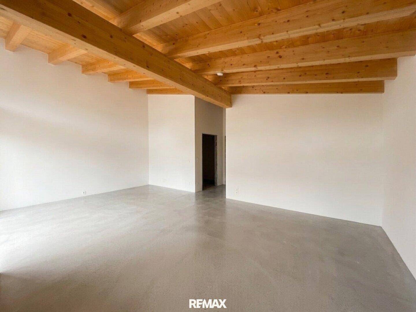 Geräumiger Innenraum mit beeindruckenden Holzdeckenbalken und einem modernen Betonboden, bereit für die Einrichtung.
