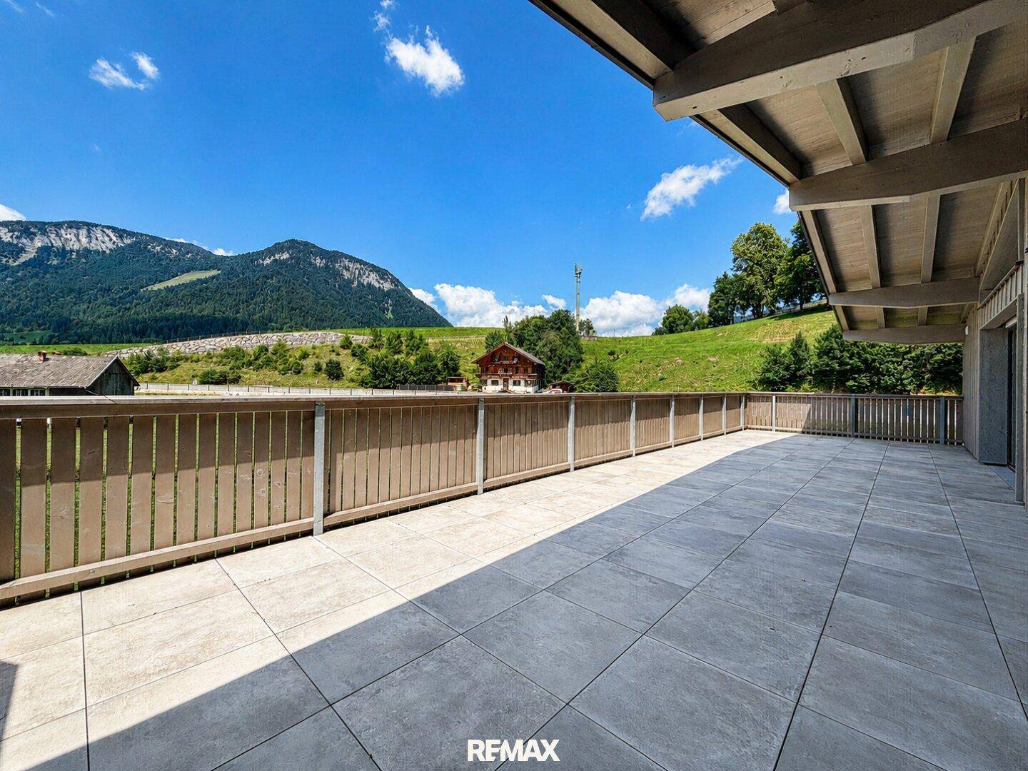 Geräumige Terrasse mit Fliesenboden und weitem Blick über die grüne Landschaft und die umliegenden Berge.