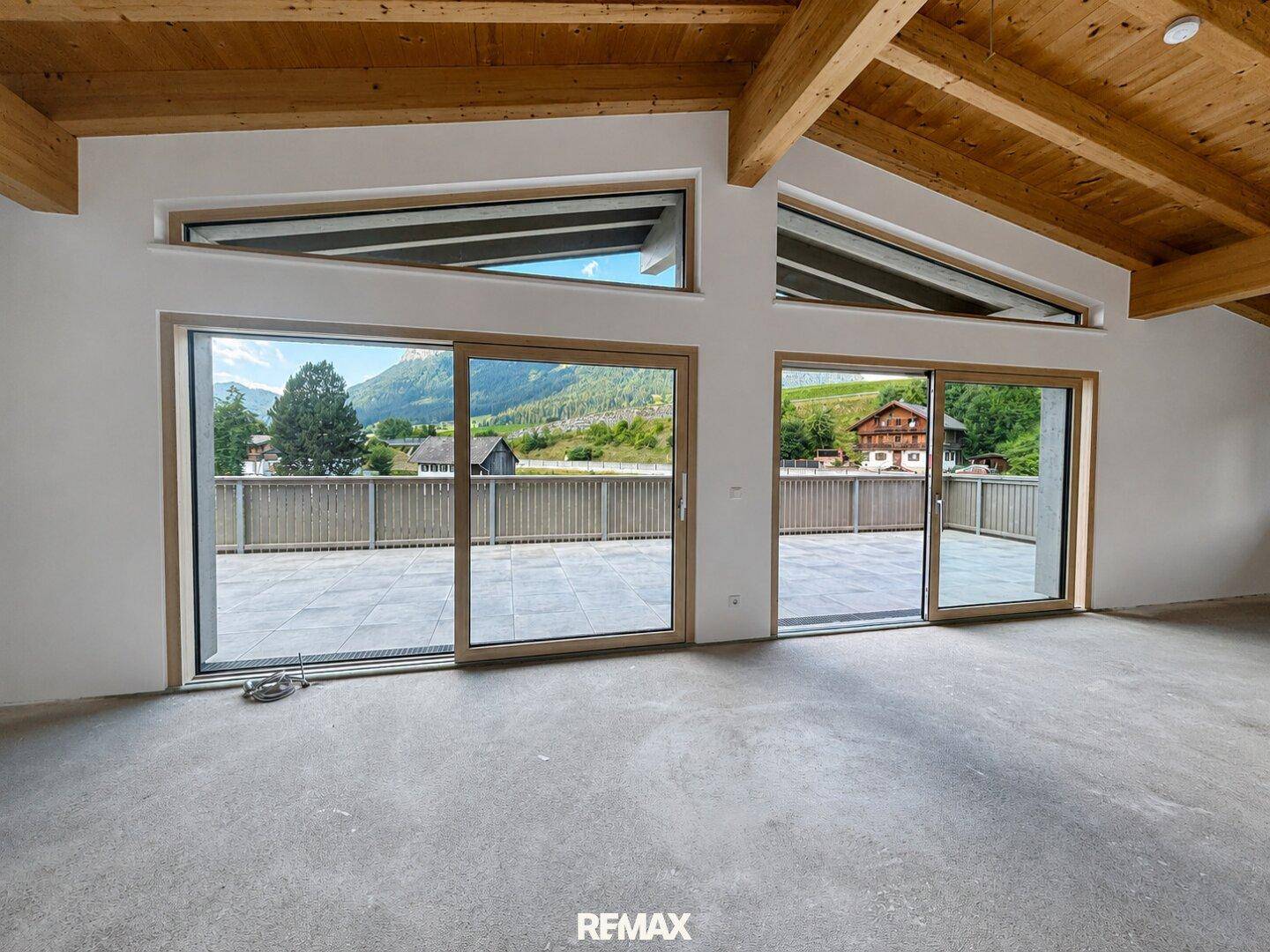 Heller Wohnbereich mit großen Glasfronten, die den Zugang zur Terrasse und den Blick auf die Berge ermöglichen.