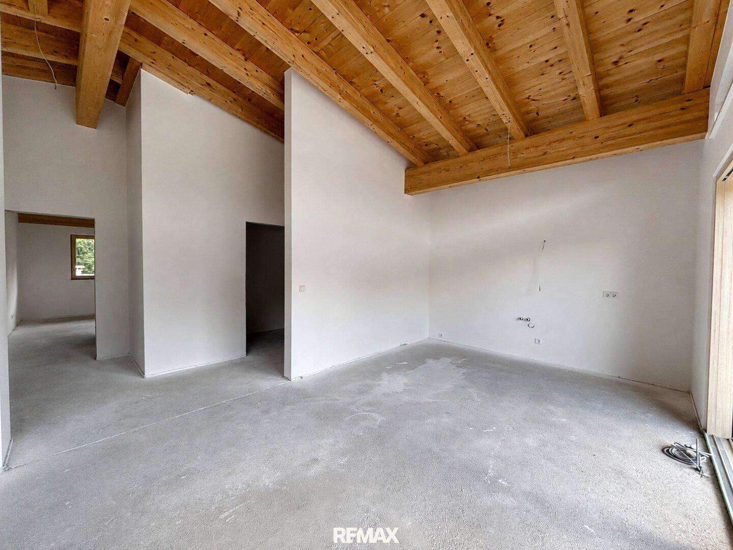 Unmöblierter Innenraum mit hohen Holzbalkendecken, Betonboden und vorbereiteten Wänden für den weiteren Ausbau.