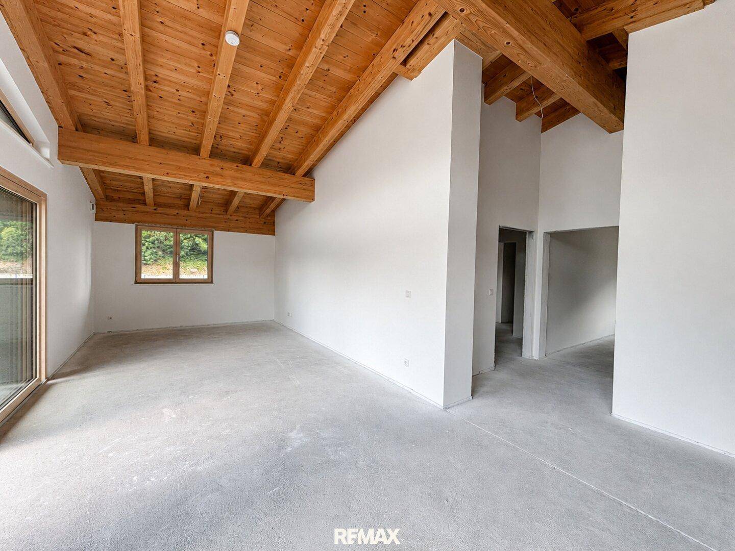 Geräumiger, unmöblierter Innenraum mit hohen Holzbalkendecken und Betonboden, bereit für den Ausbau.