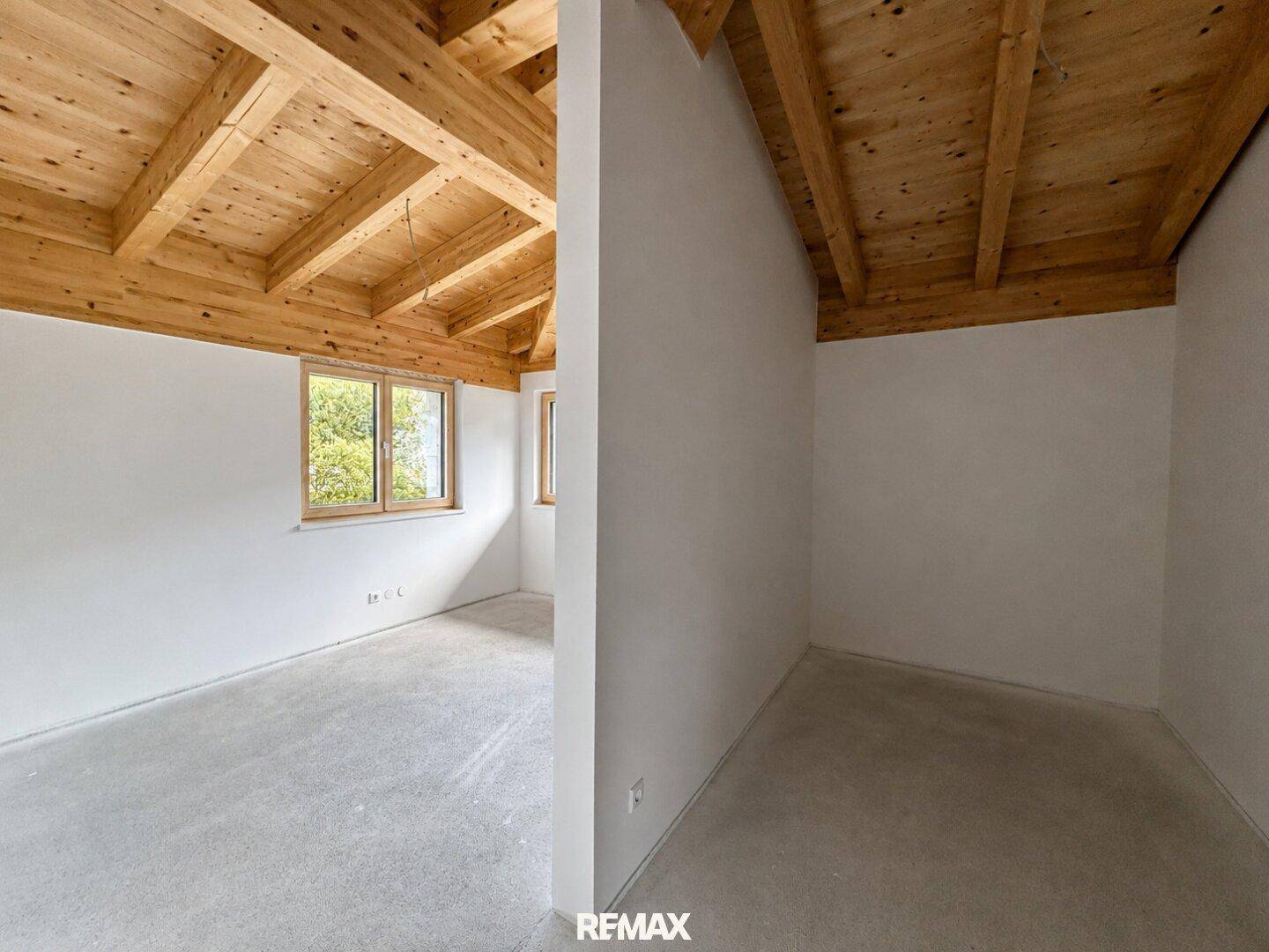 Unmöblierter Raum mit Holzbalkendecke, Betonboden und Fenster mit Blick ins Grüne, ideal als Schlafzimmer.