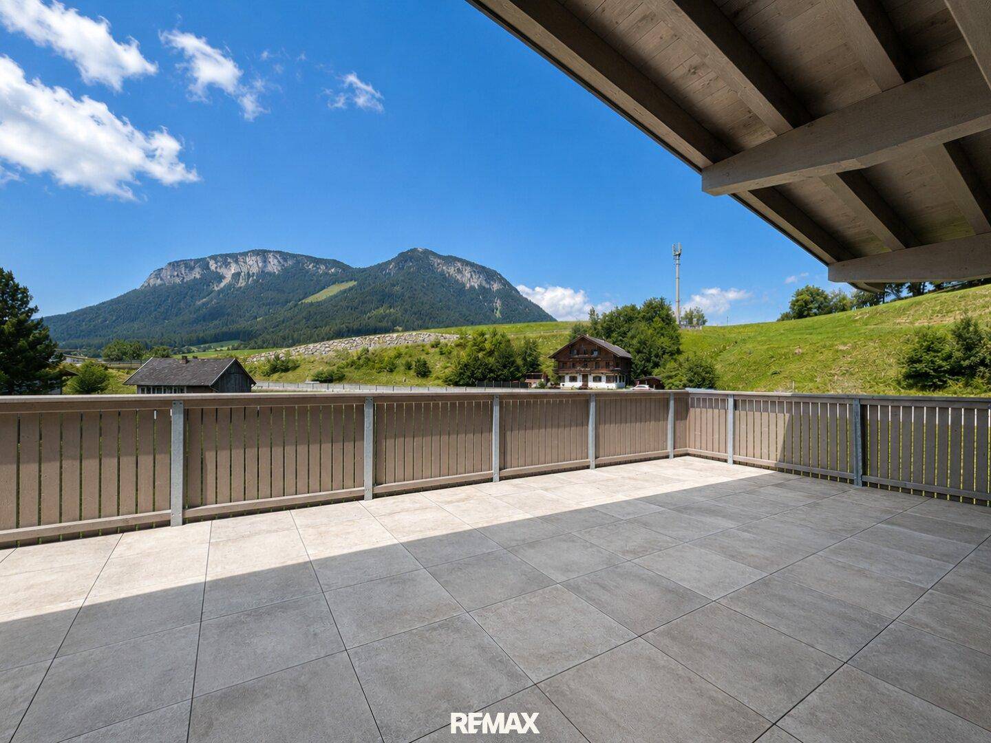 Große, sonnige Terrasse mit Fliesenboden und freiem Blick auf die majestätische Bergwelt und grüne Hügel.