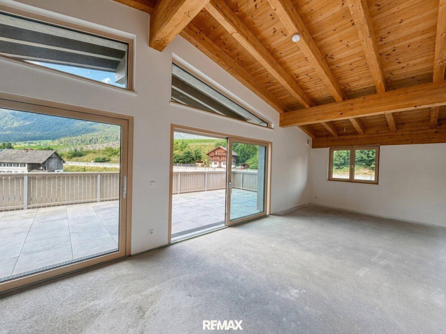 Heller, unmöblierter Wohnraum mit Holzbalkendecke, Betonboden und Zugang zur Terrasse mit Bergblick.